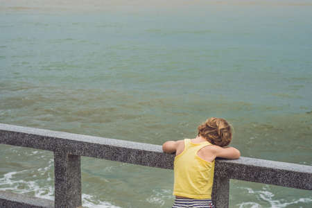 Cute boy stands on the shore watching the ocean waves.の写真素材