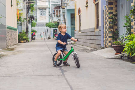 Active blond kid boy driving bicycle n the street of the city. Toddler child dreaming and having fun on warm summer day. outdoors games for children. Balance bike concept.の写真素材