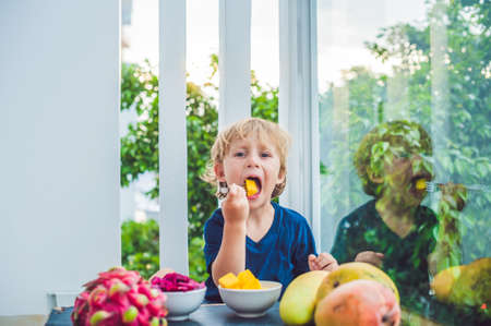 Little cute boy eating mango on the terrace.の写真素材