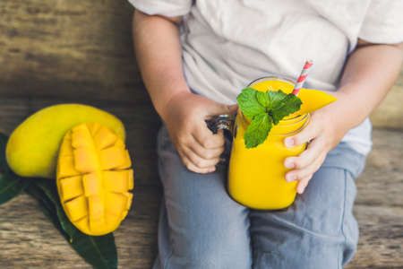 Boy drinking juicy smoothie from mango in glass mason jar with striped red straw on old wooden background. Healthy life concept, copy space.の写真素材