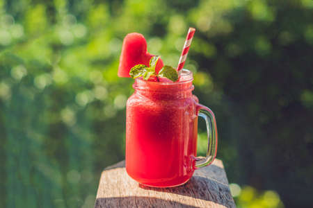 Healthy watermelon smoothie in Mason jars with mint and striped straws against the background of greenery.の写真素材