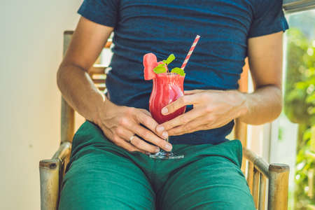 Man is holding Healthy watermelon smoothie with mint and striped straws on a wood background.の写真素材