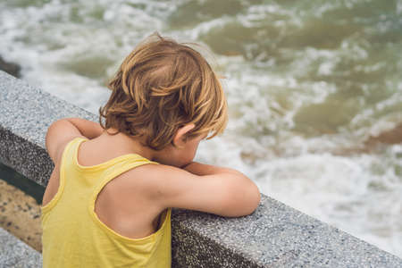 Cute boy stands on the shore watching the ocean waves.の写真素材