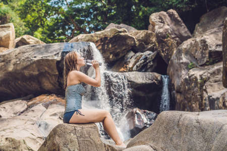 Young woman drinks water on a waterfall background.の写真素材