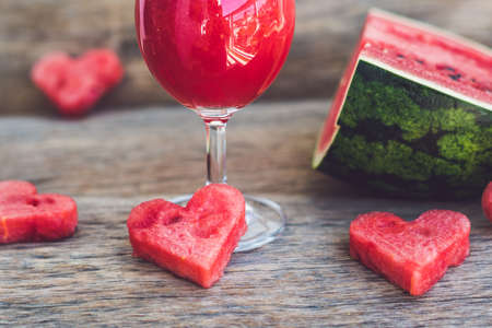 Healthy watermelon smoothie with mint, a piece of watermelon, hearts and a striped straw on a wood background.の写真素材