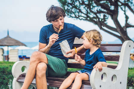 Father and son eat fried sweet potatoes in the park. Junk food concept.の写真素材