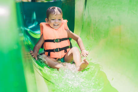 A boy in a life jacket slides down from a slide in a water park.の写真素材