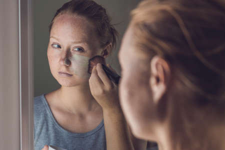 Spa Woman applying Facial green clay Mask. Beauty Treatments. Close-up portrait of beautiful girl applying facial mask.の写真素材