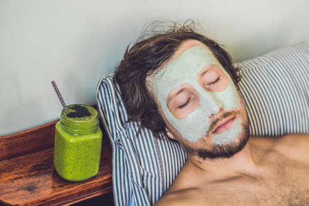 Spa man applying Facial green clay Mask. Beauty Treatments. Fresh green smoothie with banana and spinach with heart of sesame seeds. Love for a healthy raw food concept. Detox Concept.の写真素材