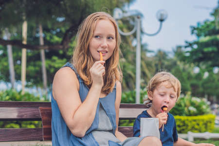 Mom and son eat fried sweet potatoes in the park. Junk food concept.の写真素材