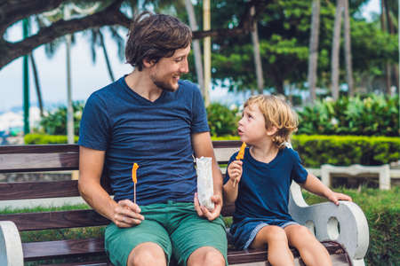 Father and son eat fried sweet potatoes in the park. Junk food concept.の写真素材