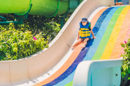 A boy in a life jacket slides down from a slide in a water park.の写真素材
