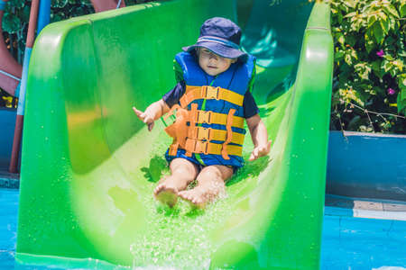 A boy in a life jacket slides down from a slide in a water park.の写真素材