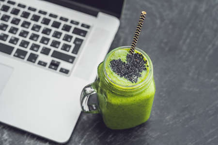Fresh green smoothie with banana and spinach with heart of sesame seeds and a laptop Love for a healthy raw food concept.の写真素材