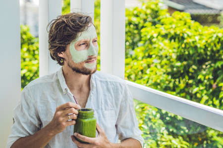 Spa man applying Facial green clay Mask. Beauty Treatments. Fresh green smoothie with banana and spinach with heart of sesame seeds. Love for a healthy raw food concept. Detox Concept.の写真素材