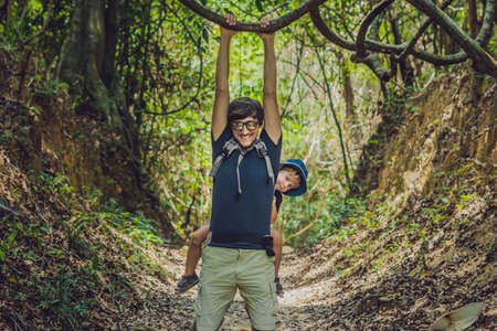 The father carries his son in a baby carrying is hiking in the forest. Tourist is carrying a child on his back in the nature of Vietnam.の写真素材