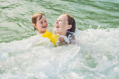 Young mother swimming and playing with male child boy in sea or ocean water sunny day outdoor on natural background, horizontal picture.の写真素材