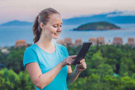 Young woman enjoys a tablet on the background of the sea.