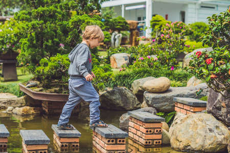 Adorable young boy with crossing river or water jumping from rock to rock. Crossing the gap, freedom, liberation, success, avoiding danger, courage concept.の写真素材
