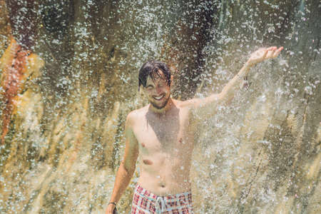 Young man relaxing under a waterfall in aquapark. Vacation conceptの写真素材