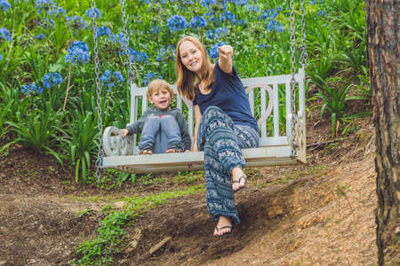 happy mother pushing laughing son on swing in a park.の写真素材