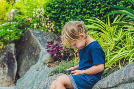 Adorable toddler boy sitting on the bench and playing with smartphone. Child learning how to use smartphone. Boy texting on the phone. - technology and lifestyle concept.の写真素材
