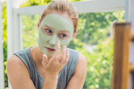Spa Woman applying Facial green clay Mask. Beauty Treatments. Close-up portrait of beautiful girl applying facial mask.の写真素材