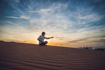 A man is pouring sand in the desert. Sand through the fingers of the concept.の写真素材