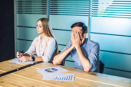 Boring presentation. Group of young business people in smart casual wear looking bored while sitting together at the table and looking away.の写真素材