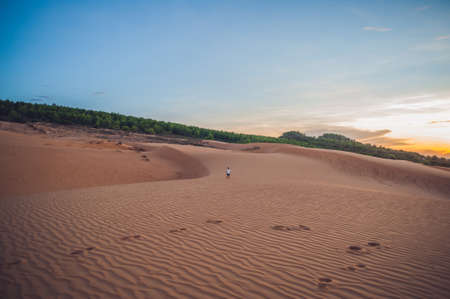 The boy runs around the red desert at dawn. Traveling in a fuss with children concept.の写真素材