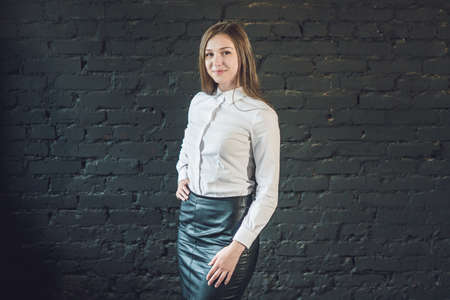 Serious thoughtful young businesswoman standing staring at the camera with folded arms over a dark grey brick background with copy space.の写真素材
