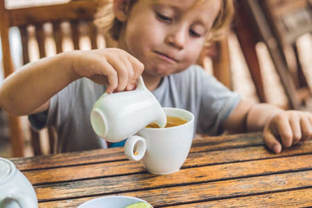 Happy nice boy pours honey into the tea in summer green garden. Portrait. outdoor.の写真素材
