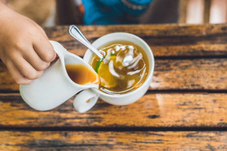 Happy nice boy pours honey into the tea in summer green garden. Portrait. outdoor.の写真素材