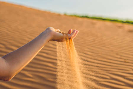 Sand slipping through the fingers of a woman's hand in the desert.の写真素材