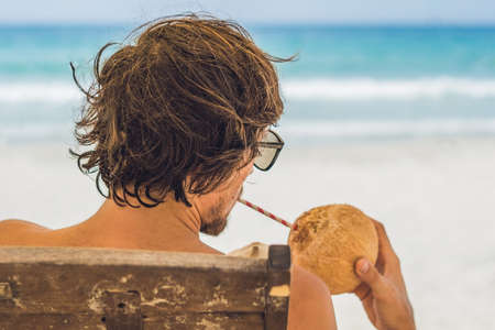 Young man drinking coconut milk on Chaise-longue on beach. Dream scape. The Benefits of Coconut Water.の写真素材