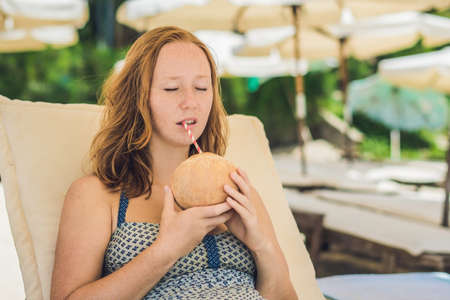 Young woman drinking coconut milk on Chaise-longue on beach. Dream scape Escape with beauty girl. The Benefits of Coconut Water.の写真素材