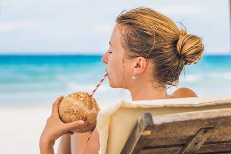 Young woman drinking coconut milk on Chaise-longue on beach. Dream scape Escape with beauty girl. The Benefits of Coconut Water.の写真素材