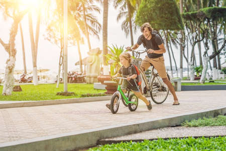 Happy family is riding bikes outdoors and smiling. Father on a bike and son on a balancebike.の写真素材