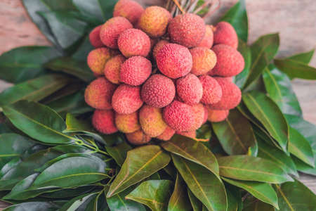 Fresh organic lychee fruit and lychee leaves on a rustic wooden background.の写真素材