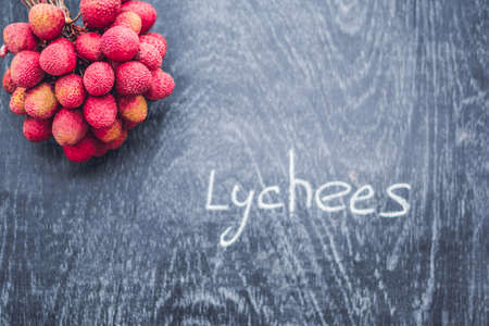 Fresh organic lychee fruit and lychee leaves on a rustic wooden background.