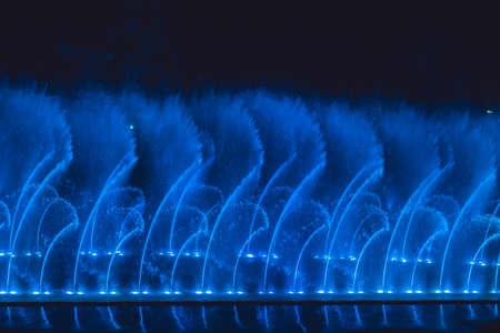 Multicolored dancing water jet fountain in the dark.の写真素材