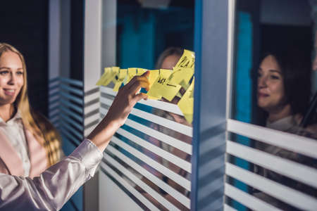 Three businesspeople discussing and planning concept. Front of glass wall marker and stickers. Startup office.の写真素材