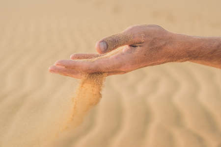 Desert, sand puffs through the fingers of a man's hand.の写真素材