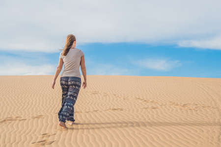 young woman in sandy desert walk alone against sunset cloudy sky. Texture of sand.の写真素材