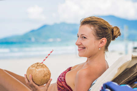 Young woman drinking coconut milk on Chaise-longue on beach. Dream scape Escape with beauty girl. The Benefits of Coconut Water.の写真素材