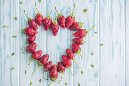 Fresh strawberries array heart shape on old wooden background.