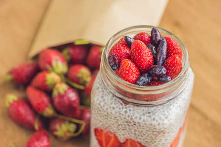 Healthy layered dessert with chia pudding, strawberry and honeysuckle in a mason jar on rustic background.の写真素材