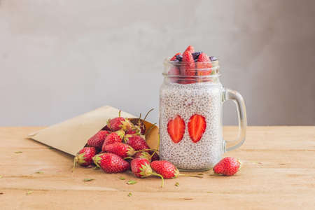 Healthy layered dessert with chia pudding, strawberry and honeysuckle in a mason jar on rustic background.の写真素材