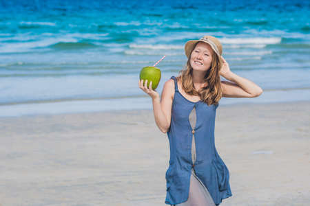 Attractive young woman drinking coconut water on the beach.