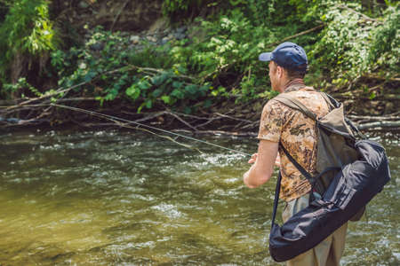 Man fishing on a mountain river with a ultralight spinning using fishing wobblers. He got his hook hooked for something.の写真素材